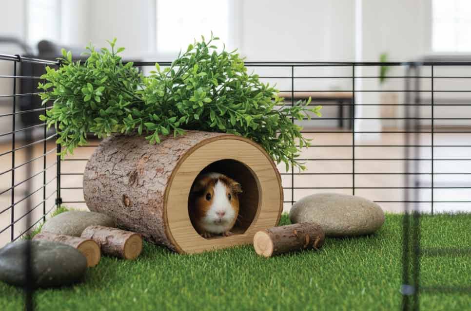 photo of a wooden guinea pig hideout nestled under artificial greenery inside a cage