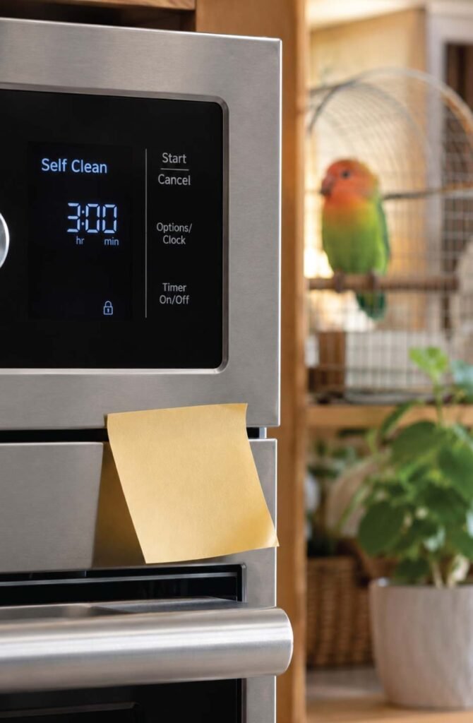 Oven control panel showing self-cleaning setting with a lovebird in a cage visible in the background