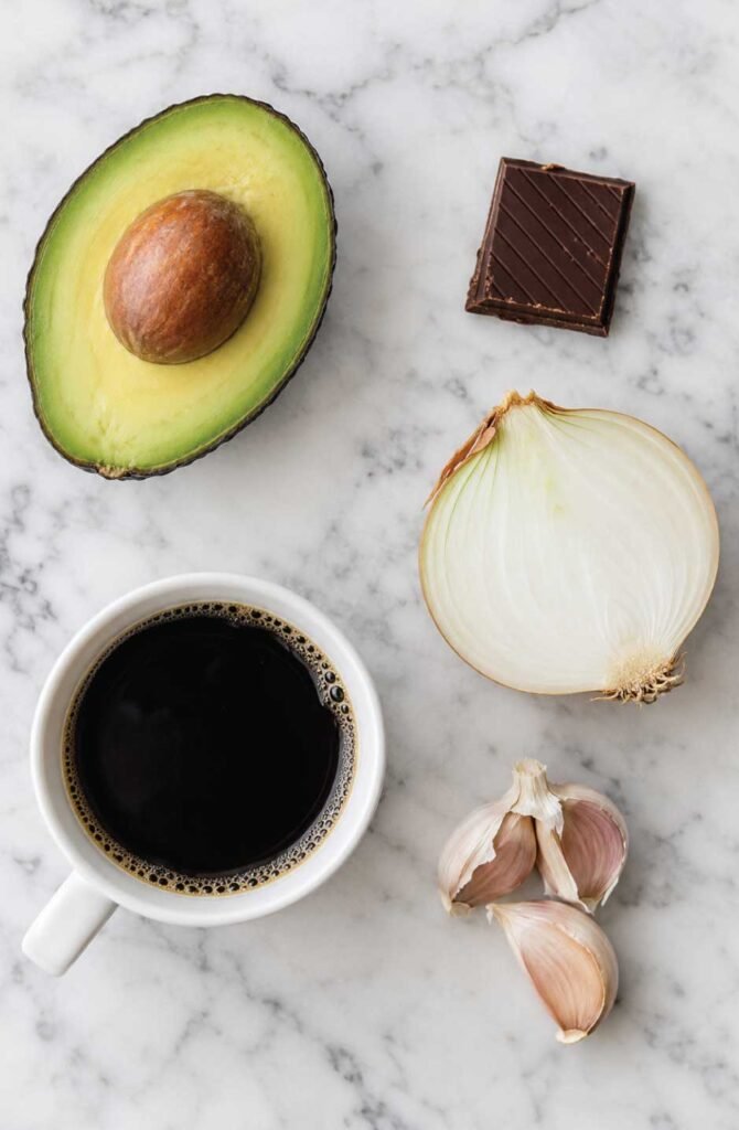 Flat-lay of toxic bird foods including avocado, chocolate, onion, coffee, and garlic on a white marble surface